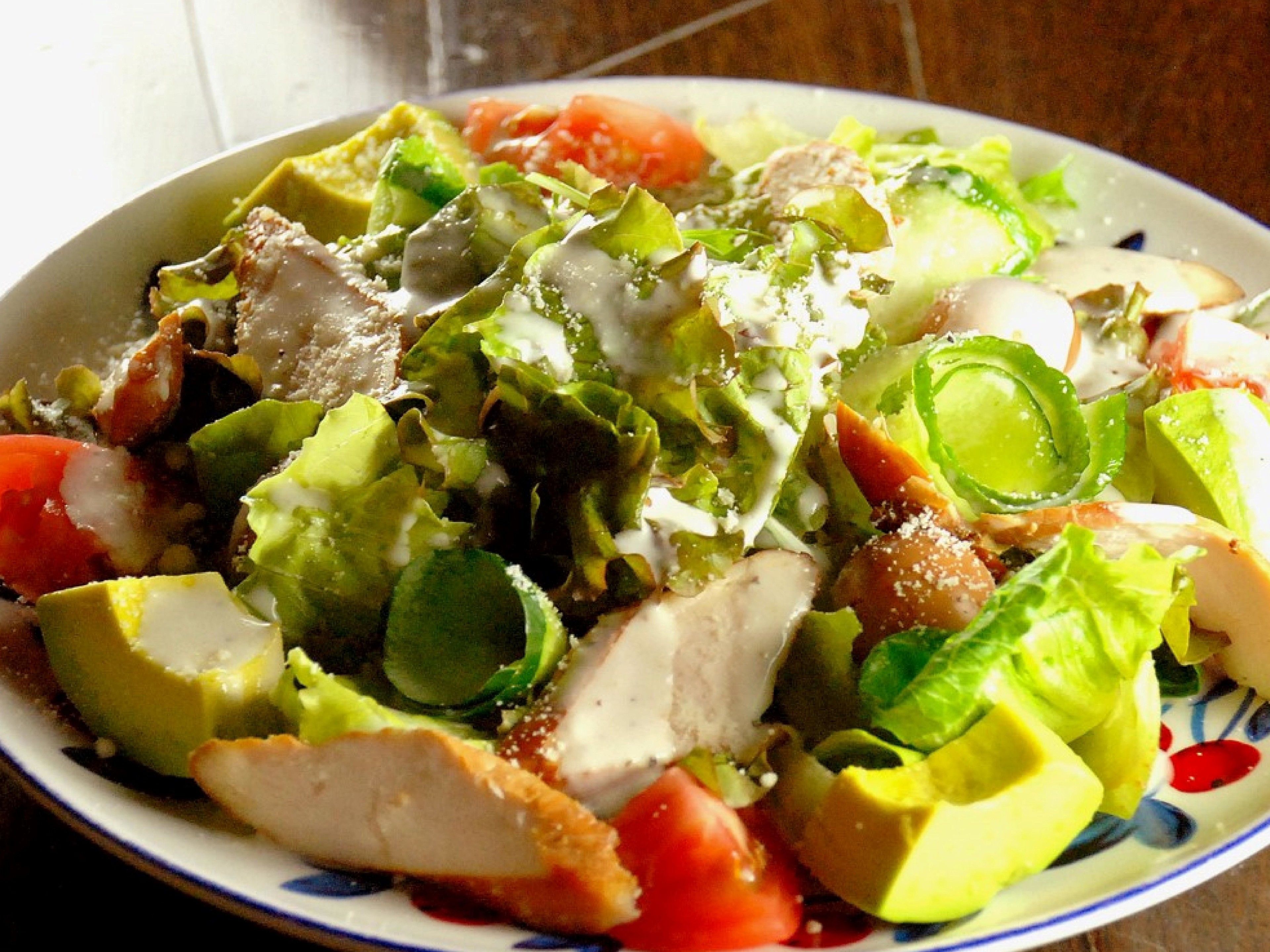 Une salade composée de divers légumes, accompagnée d’une sauce crémeuse, présentée dans une assiette.