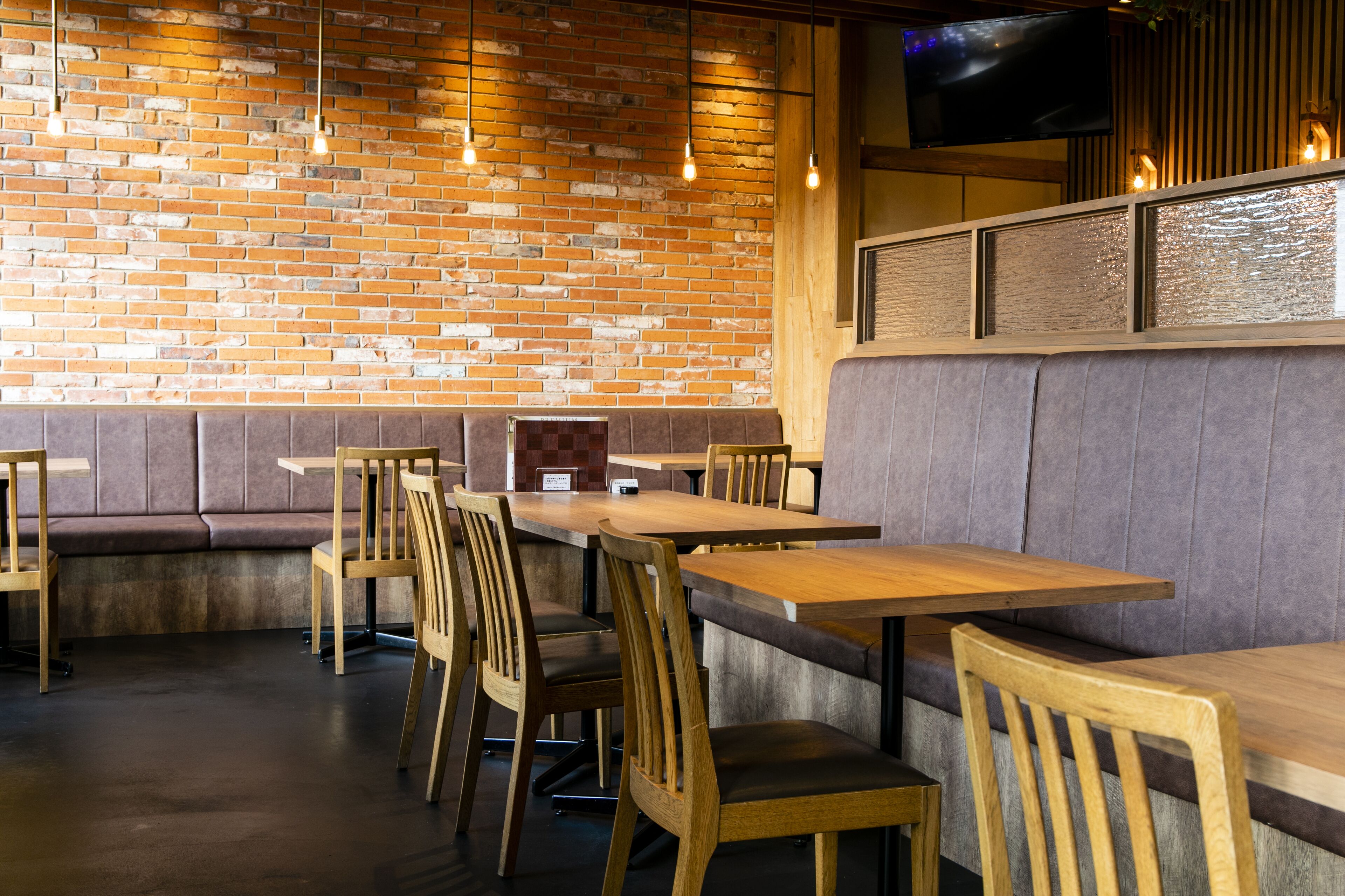 A restaurant interior with brick walls, wooden tables and chairs, and a television mounted on the wall.