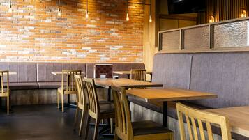 A restaurant interior with brick walls, wooden tables and chairs, and a television mounted on the wall.