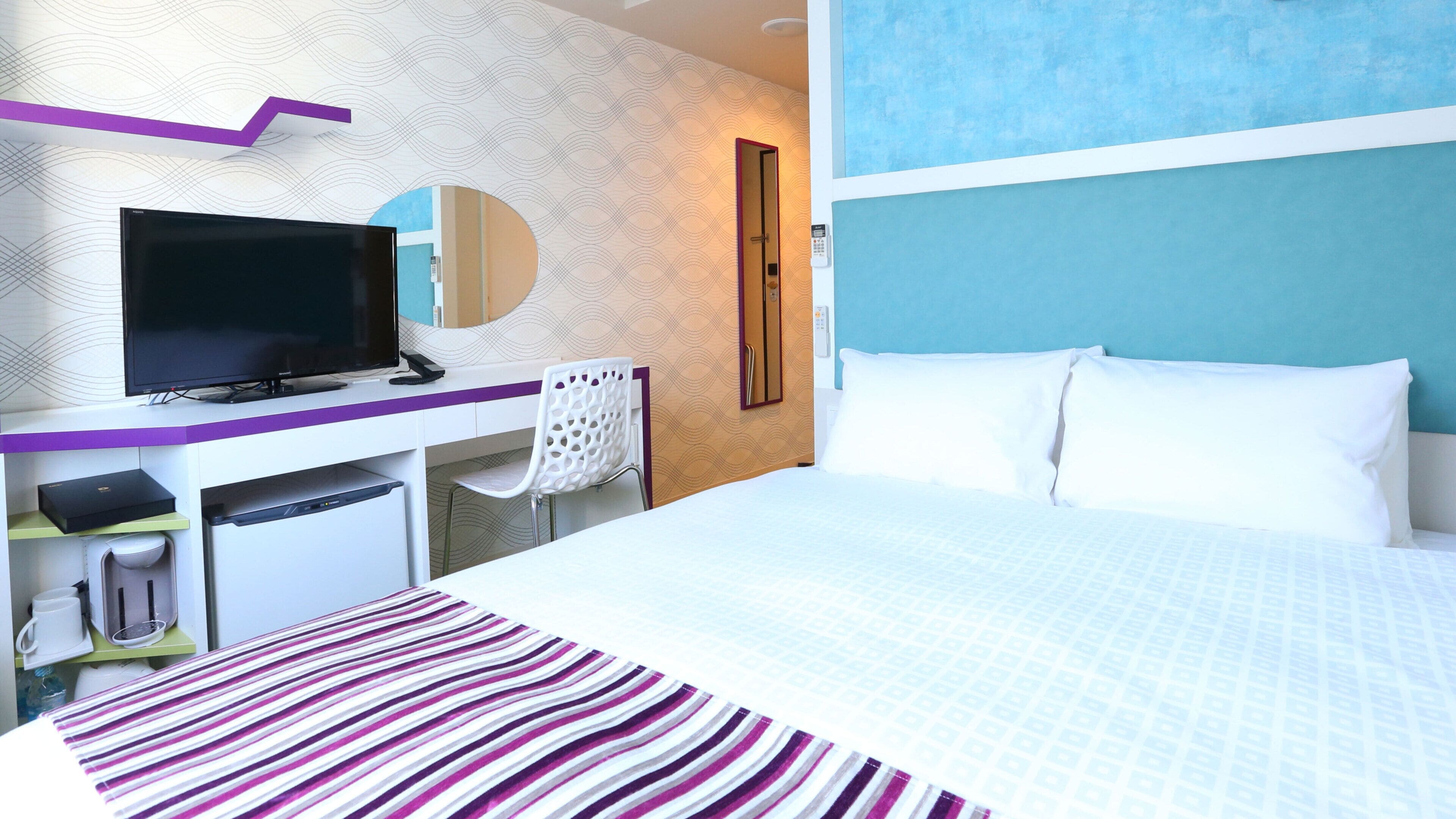 A hotel room with a bed, a desk with a TV, a mirror, and a phone.