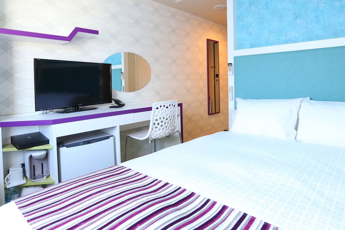 Une chambre d’hôtel avec un lit, un bureau avec une télévision, un miroir et un téléphone.