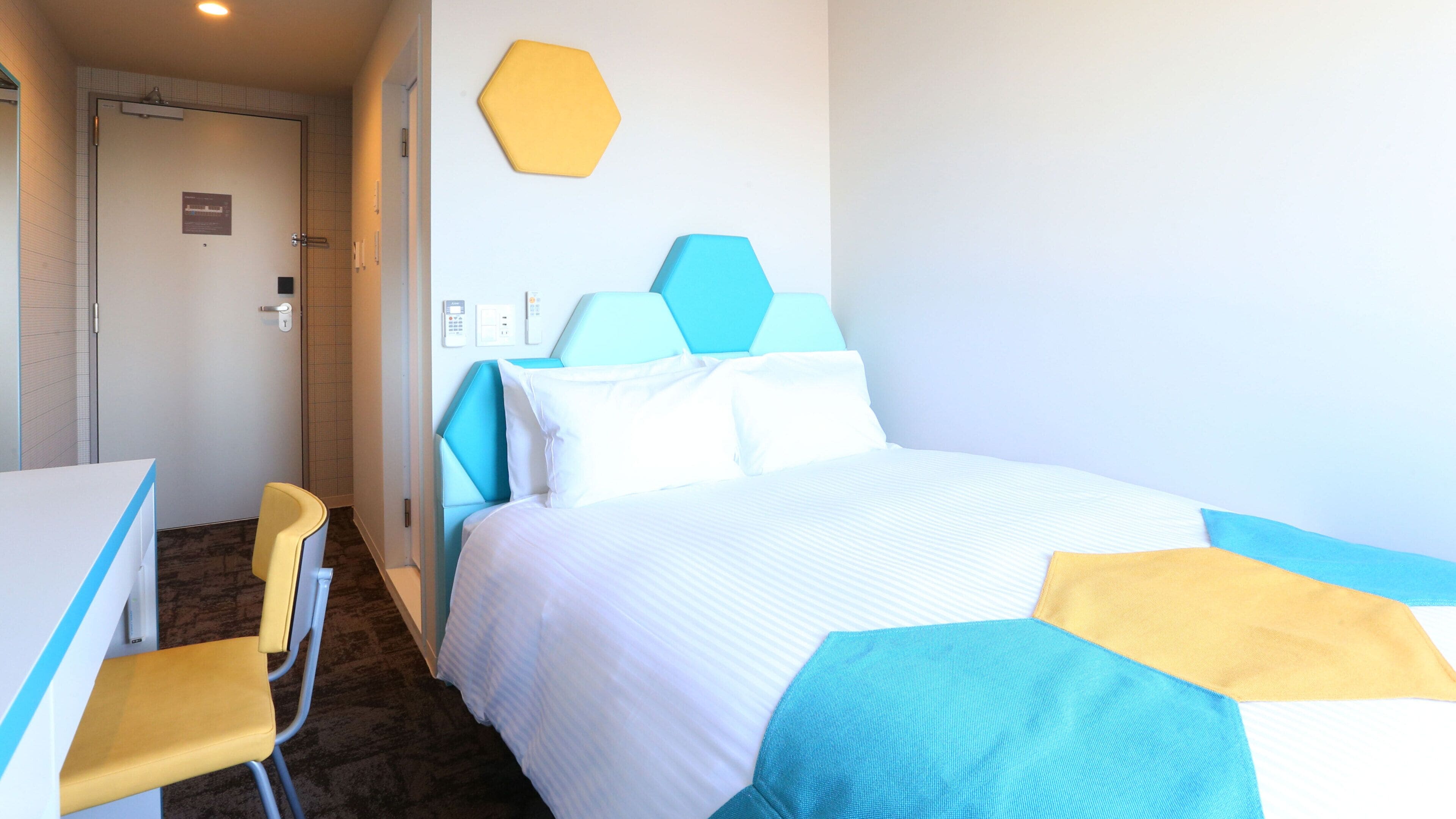 A hotel room with a bed, a desk, a chair, and a bathroom door.