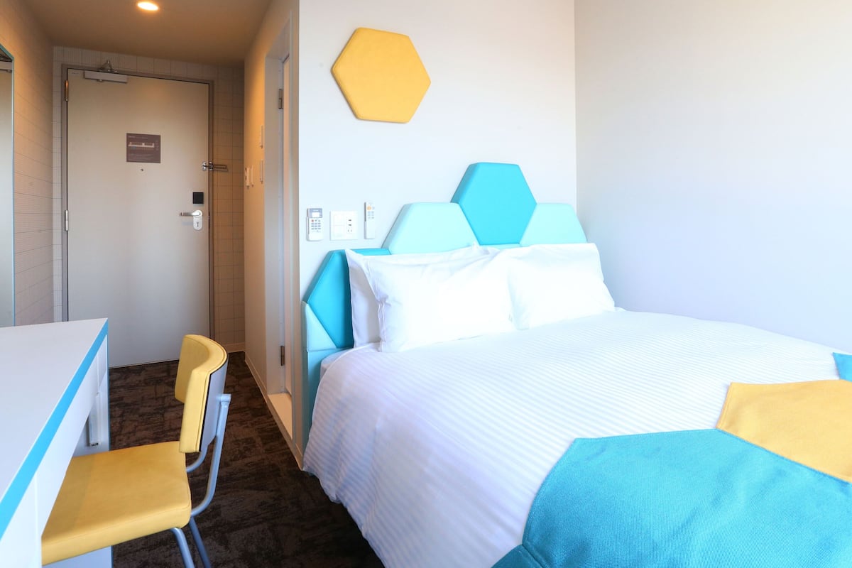 Une chambre d’hôtel avec un lit, un bureau, une chaise et une porte de salle de bain.