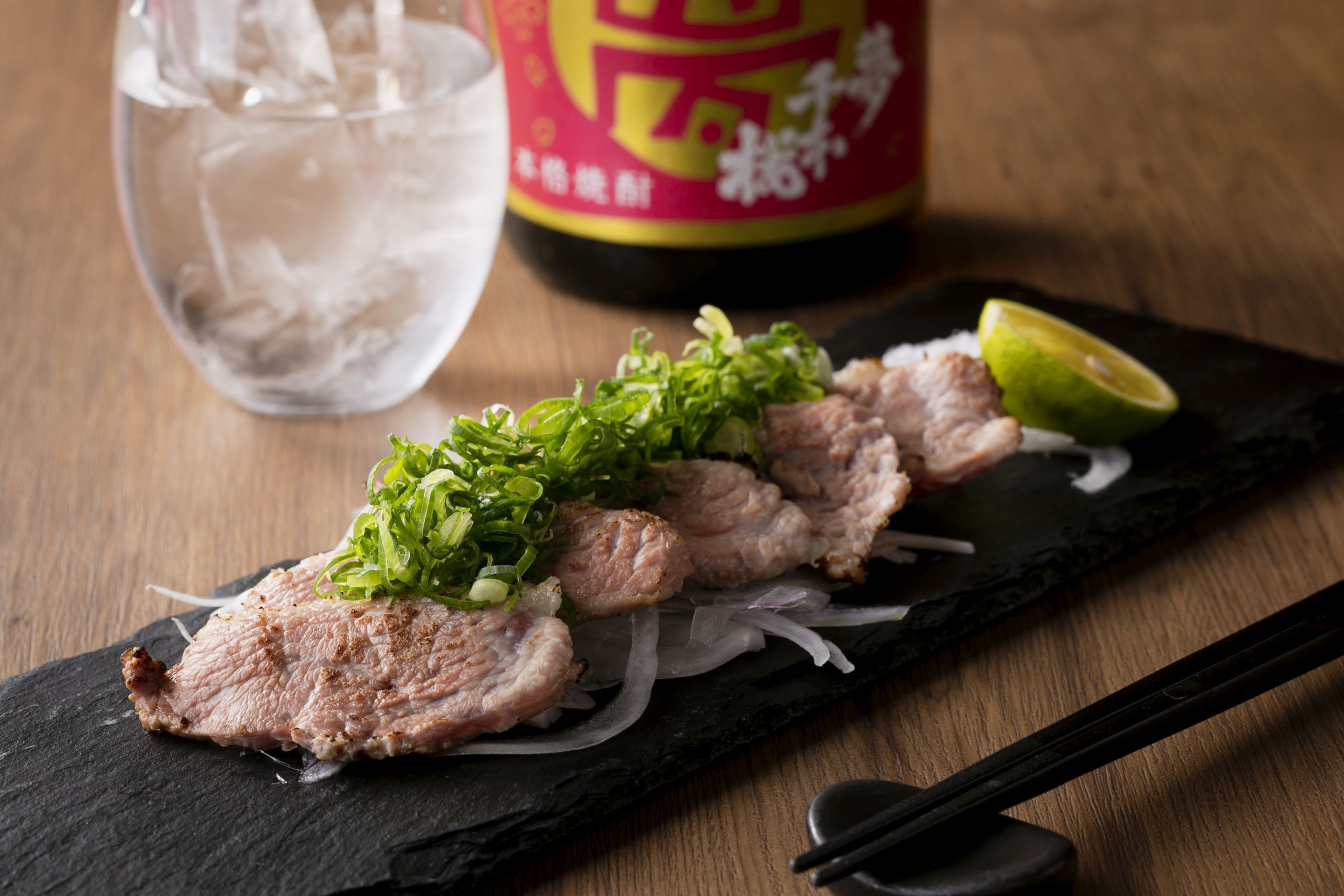 A slice of meat with green onions and a lime wedge on a black slate plate.