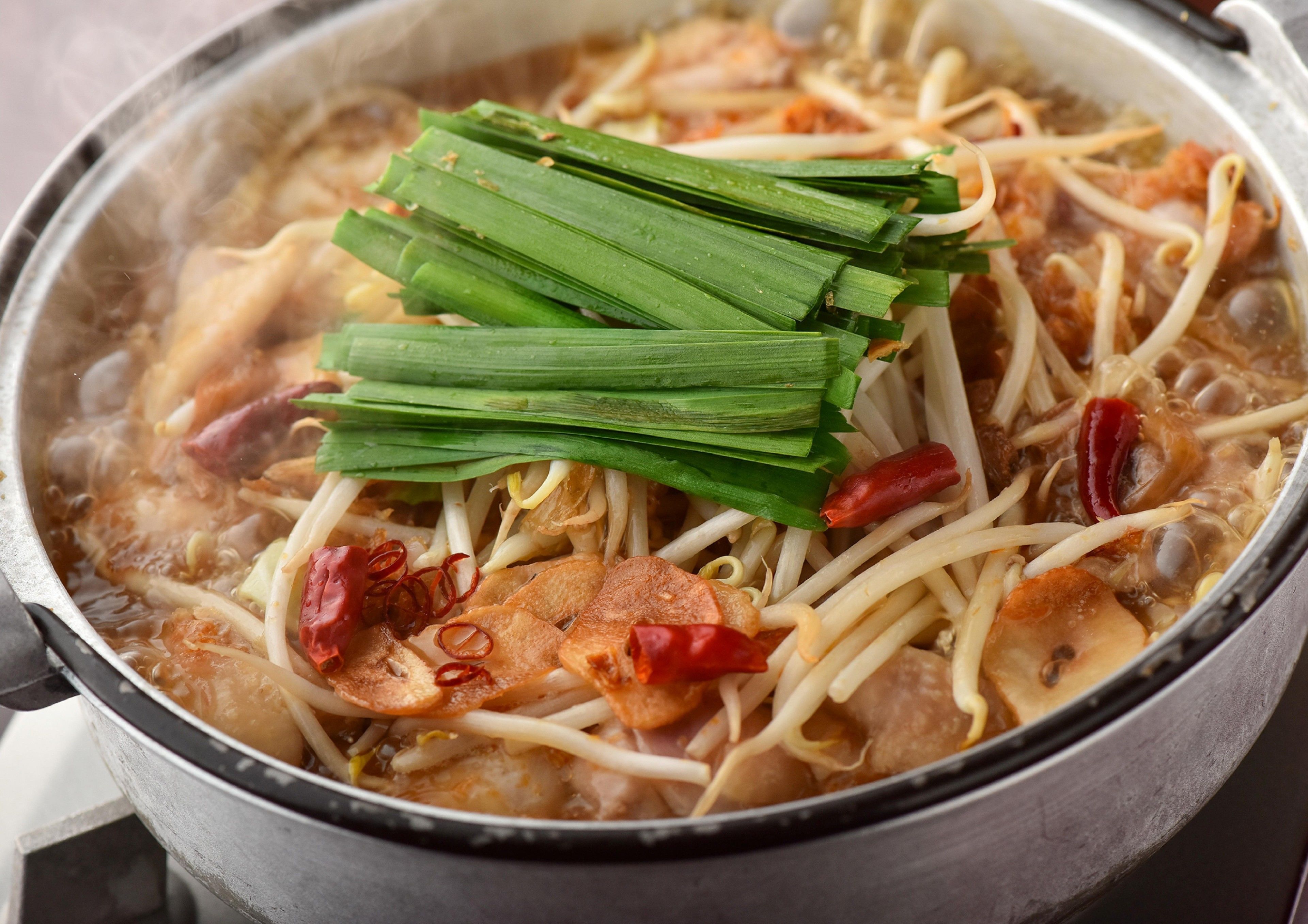 A pot of soup with noodles, vegetables, and red chili peppers.