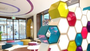 A modern interior with colorful hexagonal partitions, comfortable seating, and large windows offering views of the street. - KOKO HOTEL Higashiosaka (Higashi-osaka)