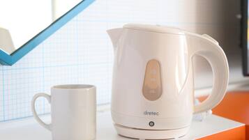 Une bouilloire électrique blanche et une tasse blanche sont posées sur un plan de travail blanc bordé d’une ligne orange.