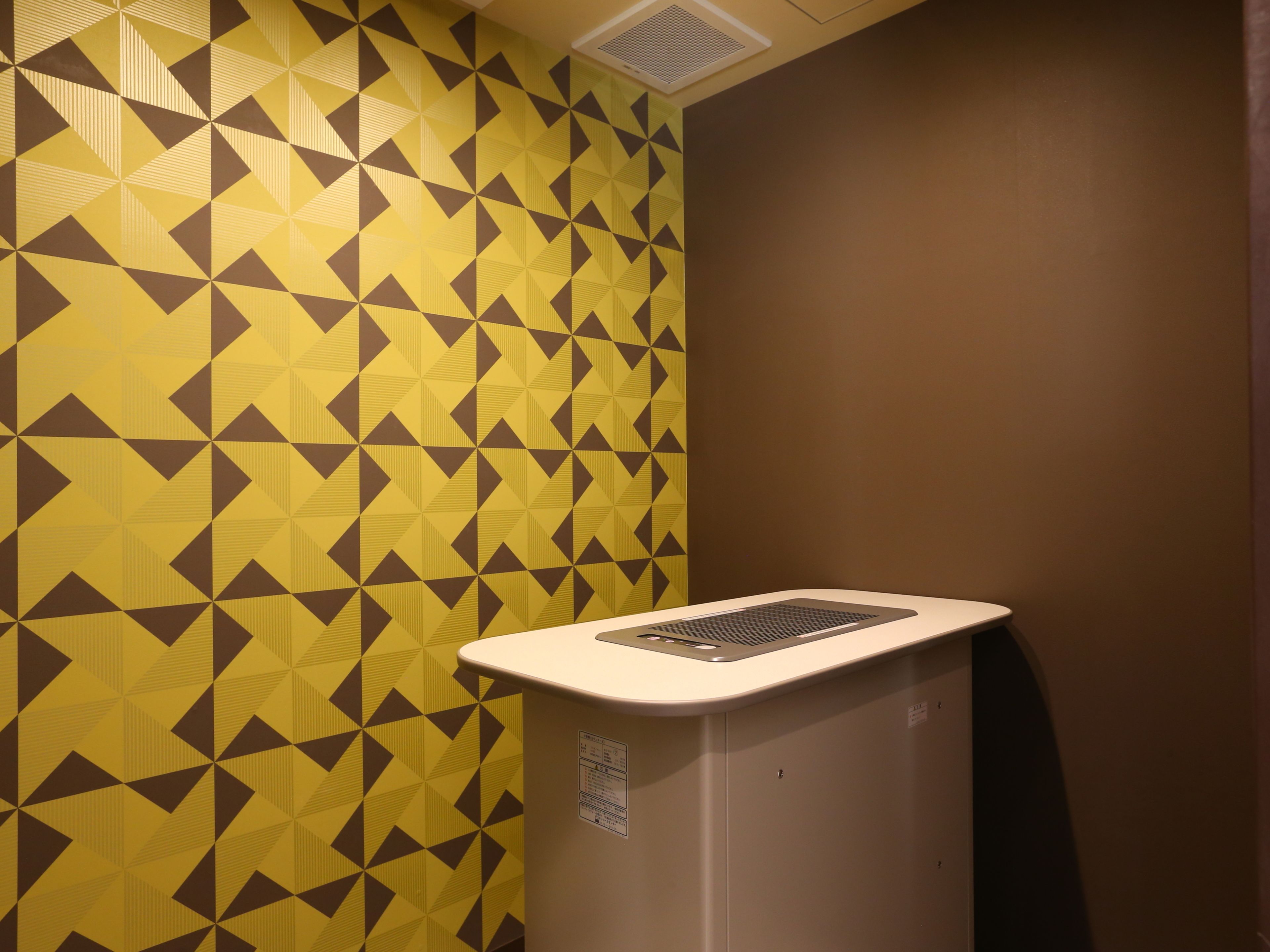 A restroom with a geometric patterned wall, a white sink, and a ventilation grille on the ceiling.