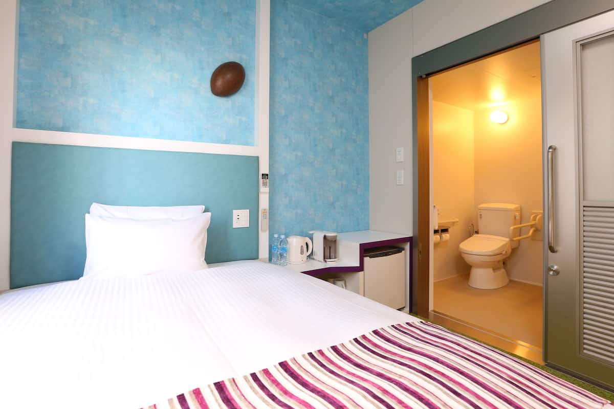 Une chambre d’hôtel comprenant un lit, une salle de bain avec des toilettes et un lavabo, ainsi qu’un espace douche.
