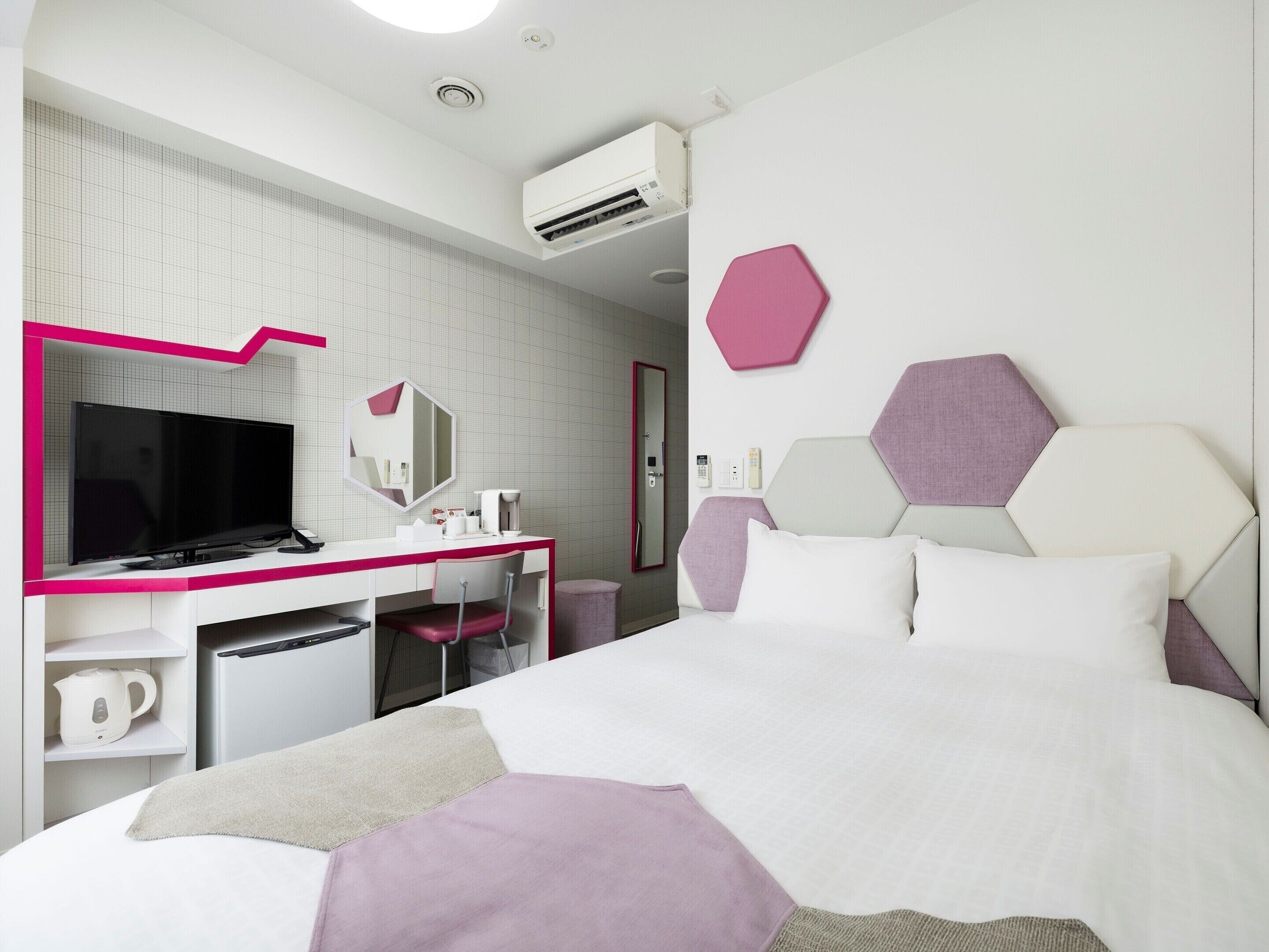 A modern hotel room with a large bed, a desk with a flat-screen TV, a mirror, and a wall-mounted air conditioner.