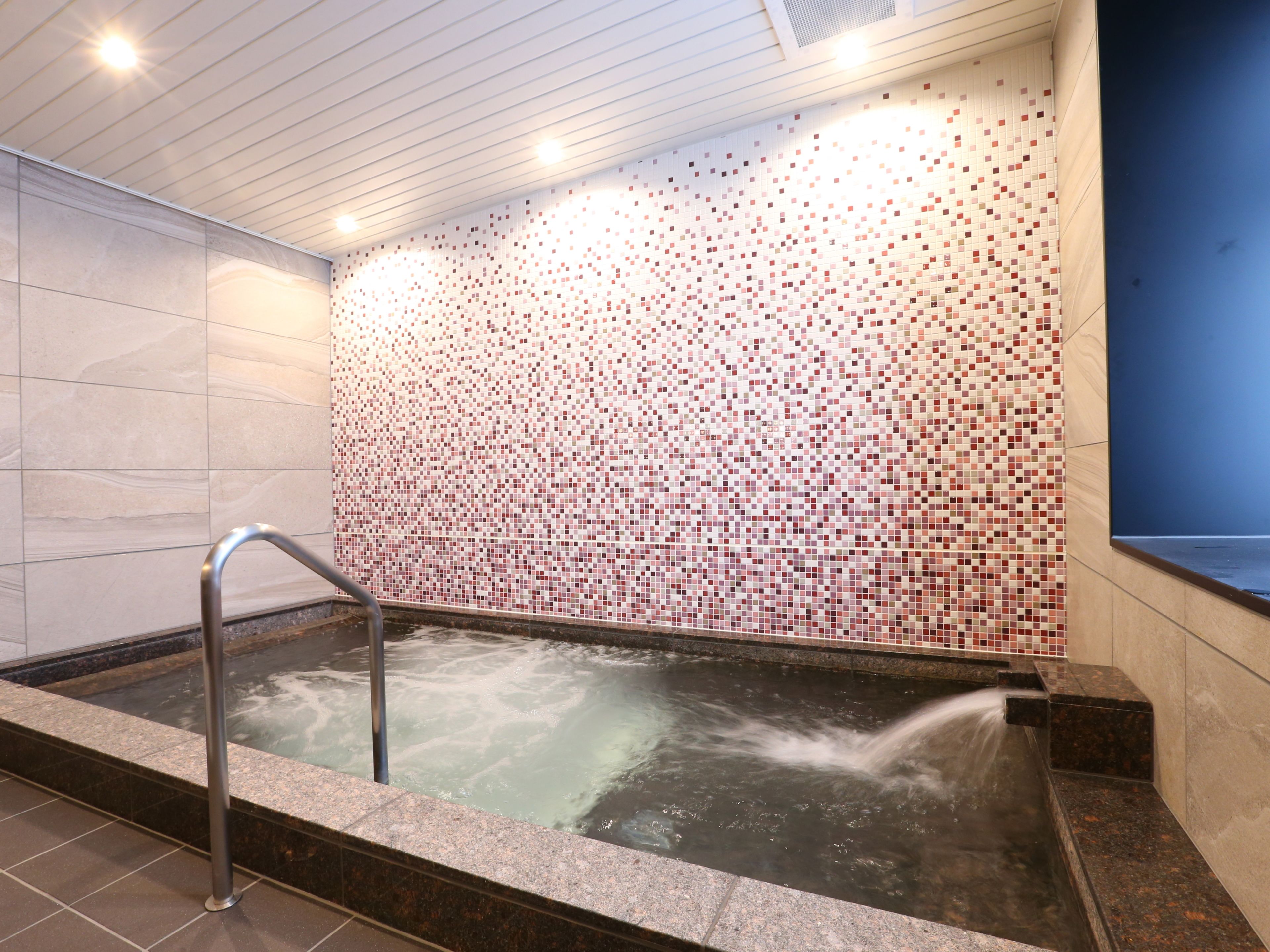 Un espace de bien-être avec un mur carrelé, un jacuzzi et une rambarde en métal.