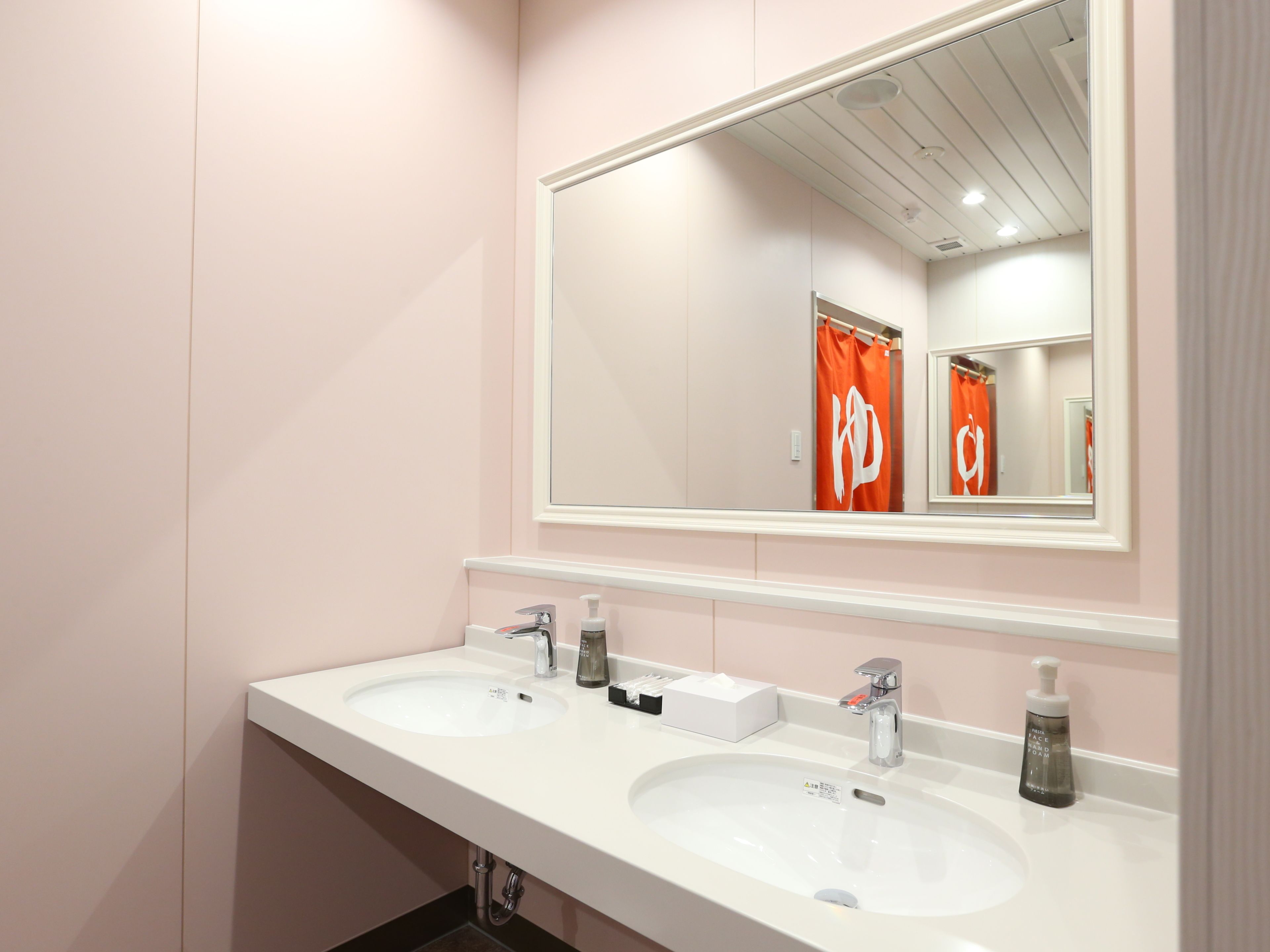 Une salle de bain avec deux lavabos, un miroir et un rideau de douche orné d’un logo.