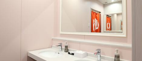 Une salle de bain avec deux lavabos, un miroir et un rideau de douche orné d’un logo.