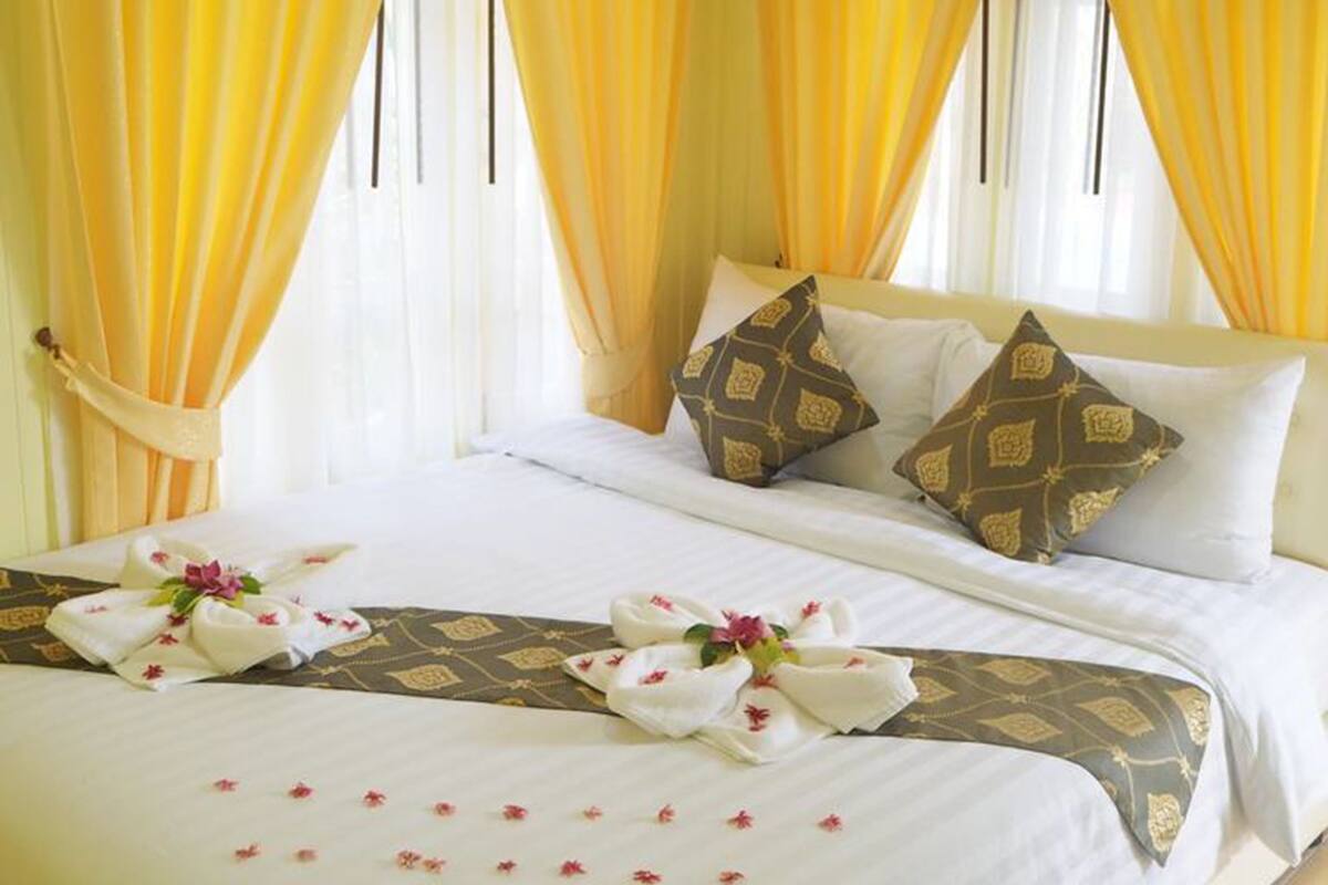 A hotel room with a bed, yellow curtains, and decorative pillows.