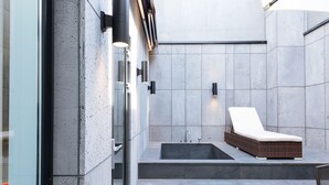 A modern bathroom with a large bathtub, a sun lounger, and a glass door leading to a pool area. - Boutique Hotel XYM Pyeongtaek (Pyeongtaek)