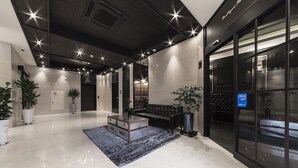 A modern lobby with a polished floor, a vintage trunk as a coffee table, and a black leather sofa. - Boutique Hotel XYM Pyeongtaek (Pyeongtaek)