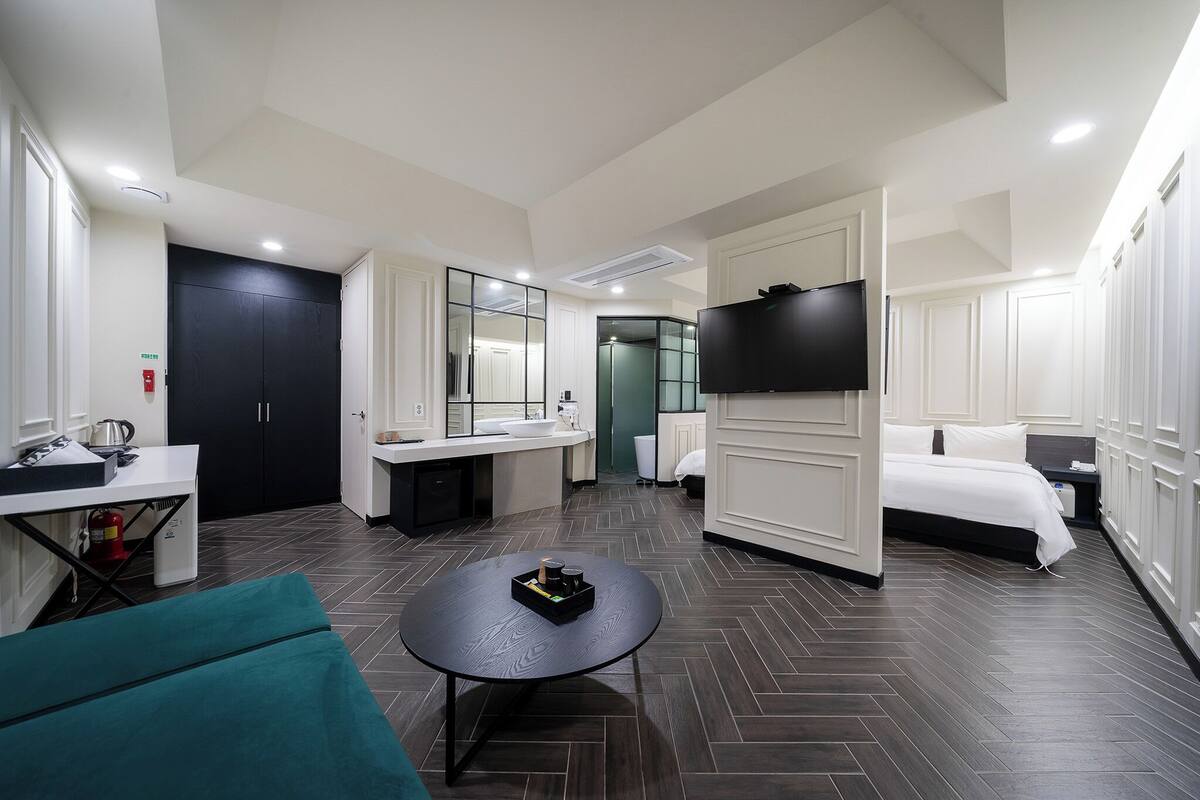 A hotel room with a bed, a TV, a desk with a chair, a small table, and a mirror.