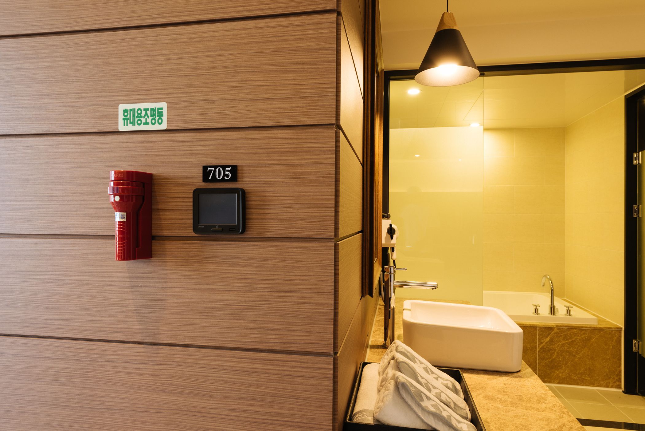 Ein Hotelzimmer mit einer Holzwand, einem digitalen Schloss, einem roten Schlüsseltaschenhalter, einem weißen Waschbecken und einer Badewanne.
