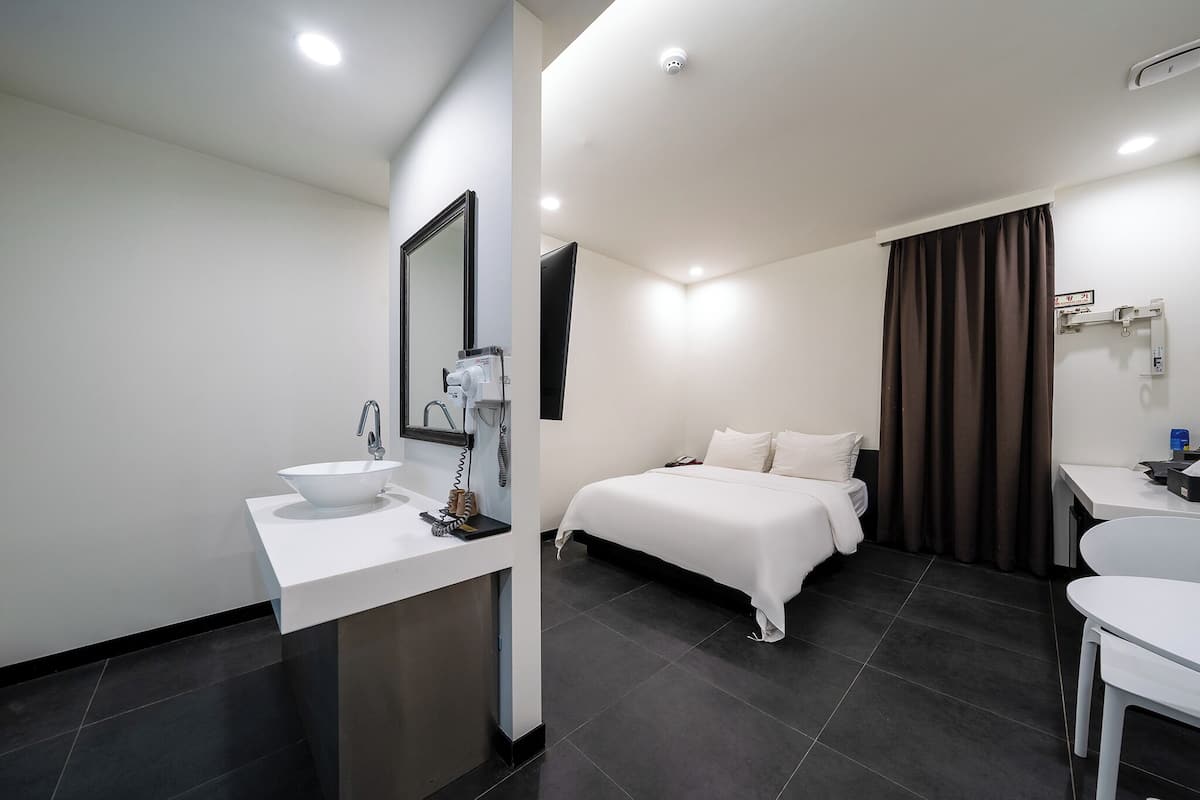 A modern hotel room with a white bed, a white sink, and a large mirror.