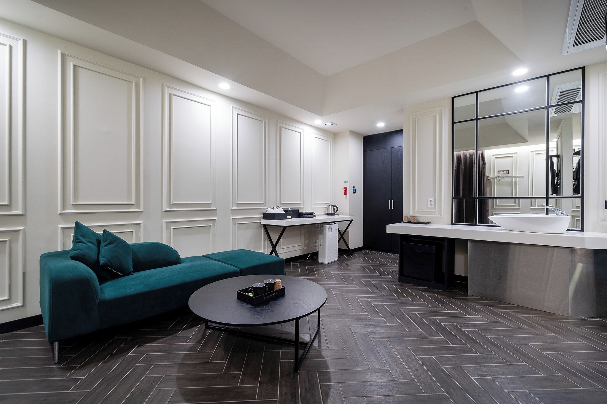 Une chambre d’hôtel moderne équipée d’un canapé, d’une petite table, d’un coin cuisine et d’un grand miroir.