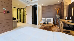 A modern hotel room with a large bed, a small round table, a sofa with pillows, a coat rack, and a desk with a kettle. - Boutique Hotel XYM Pyeongtaek (Pyeongtaek)