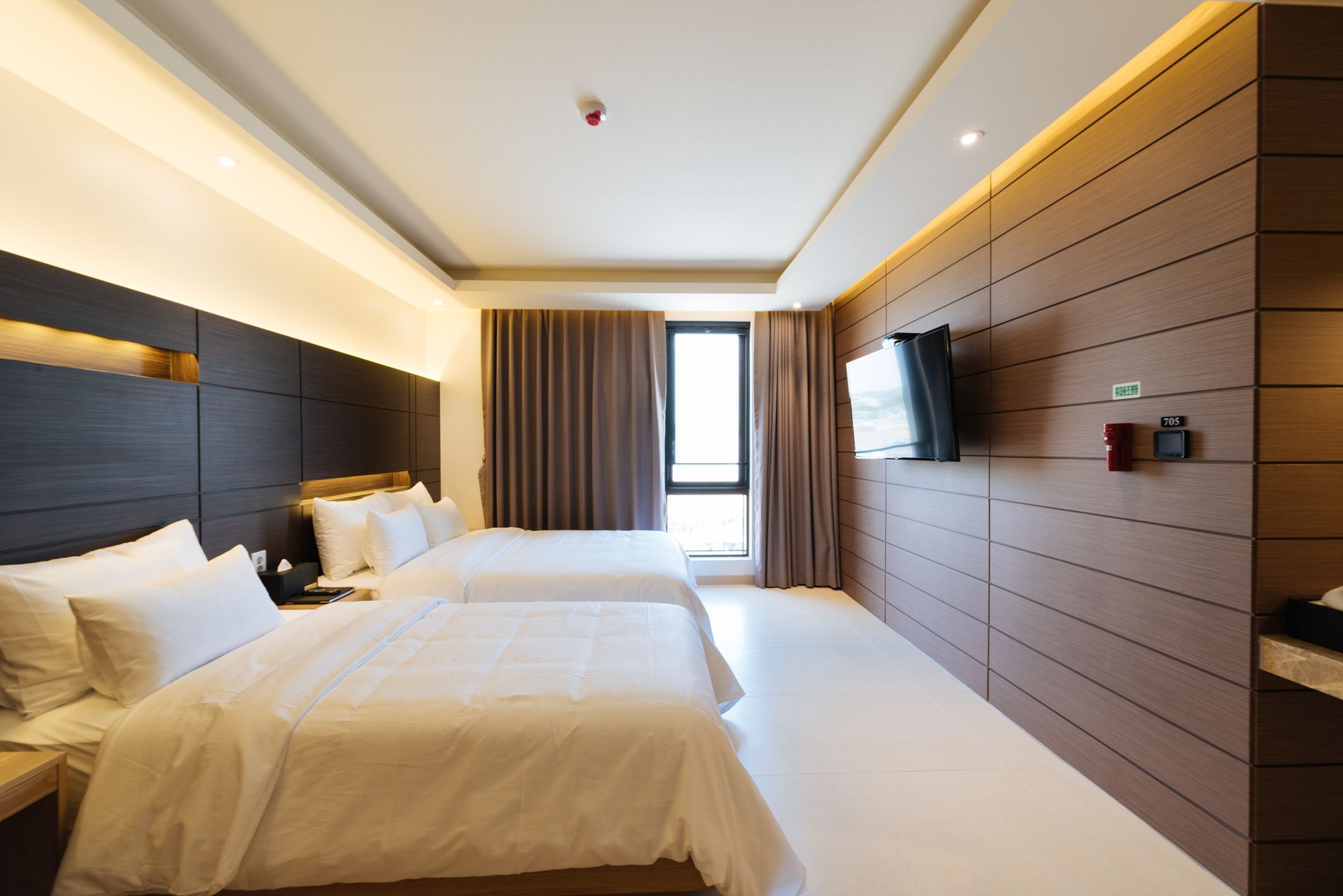 A hotel room with two beds, a TV mounted on the wall, and a window with curtains.
