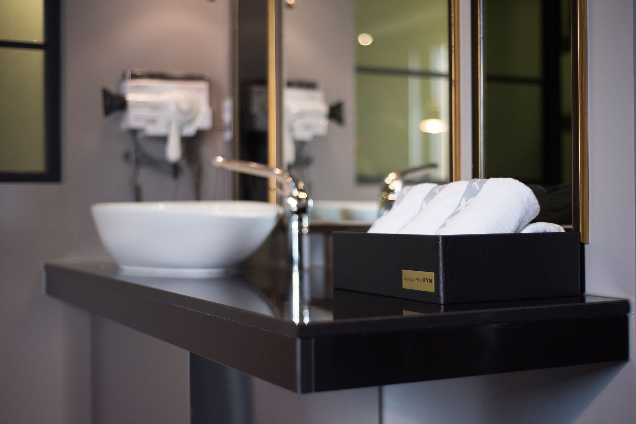 A modern bathroom with a large mirror, a white sink, and a black towel box on the counter.