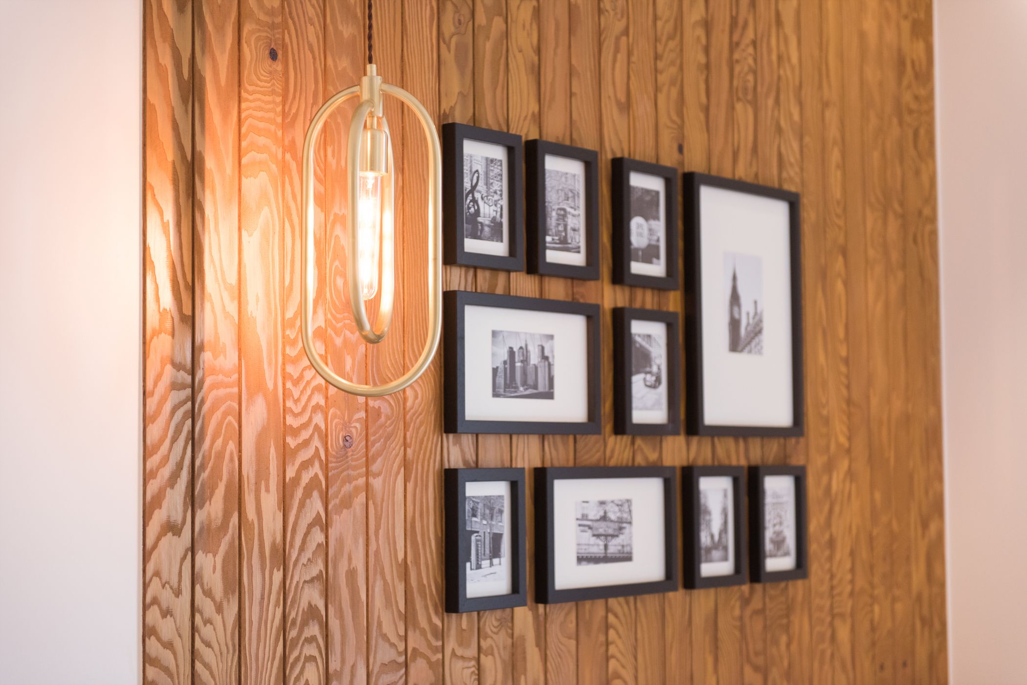A wall with framed photographs and a hanging light fixture.