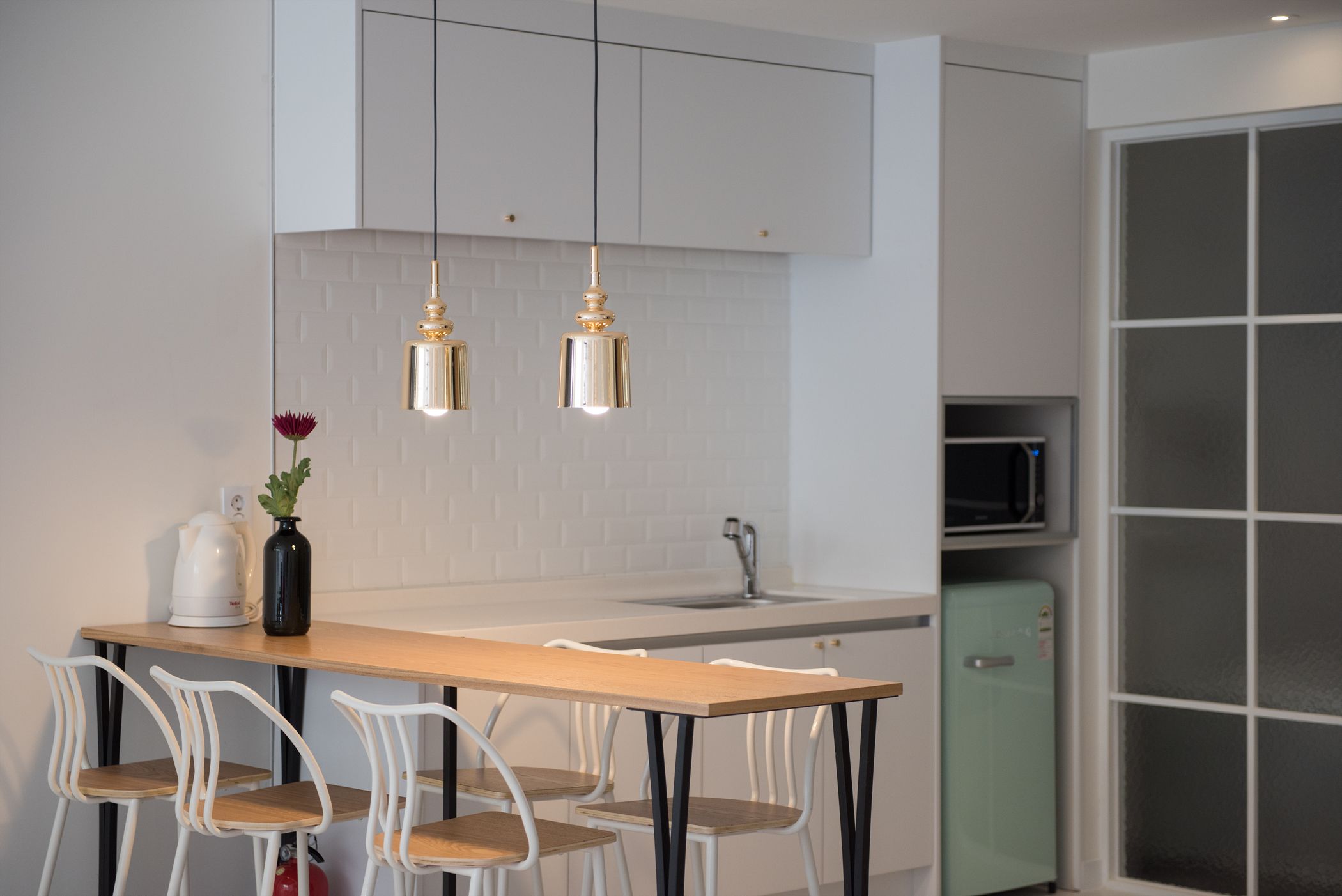A modern kitchen with a wooden table, white chairs, and pendant lights.