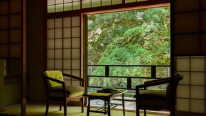 A traditional Japanese room with tatami flooring, a low table, and two chairs. A large window reveals a lush garden. - Kibune Hiroya (Kyoto)
