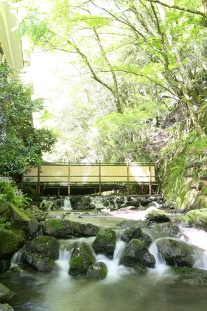 A serene waterfall with moss-covered rocks and a traditional wooden bridge in the background. - Kibune Hiroya (Kyoto)