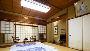 A traditional Japanese room with tatami flooring, a bed with a blue floral bedspread, sliding doors, and a television. - Kibune Hiroya (Kyoto)