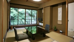 A traditional Japanese room with tatami flooring, a low table, a cushioned bench, a television, and a large window offering a view of greenery. - Kibune Hiroya (Kyoto)