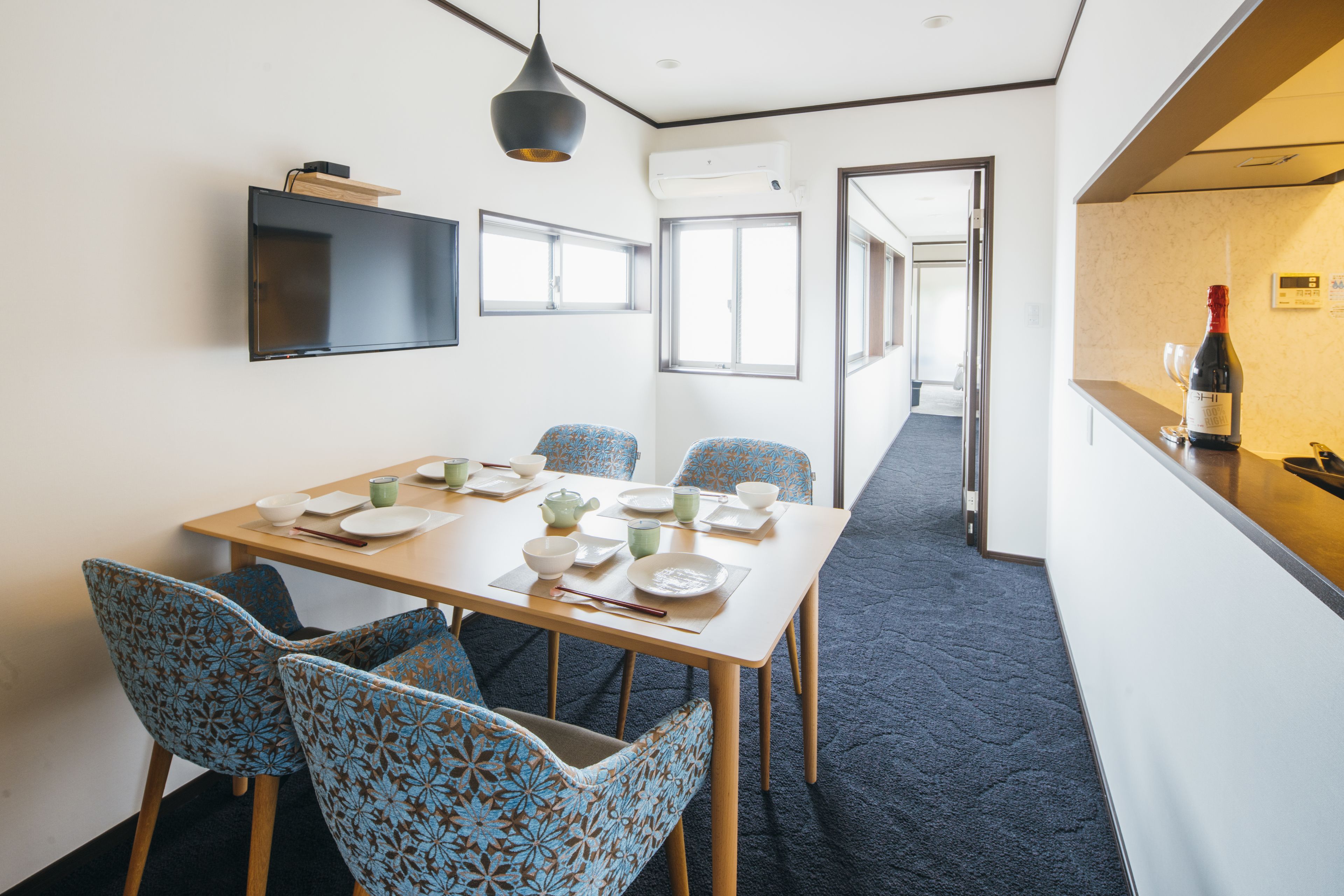 Een moderne hotelkamer met een zithoek, met een houten tafel, gestreepte stoelen en een flatscreen televisie aan de muur.