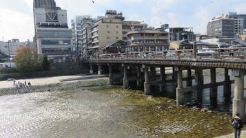 Un paseo a orillas del río con un sendero de piedra, un puente de madera y edificios al fondo.