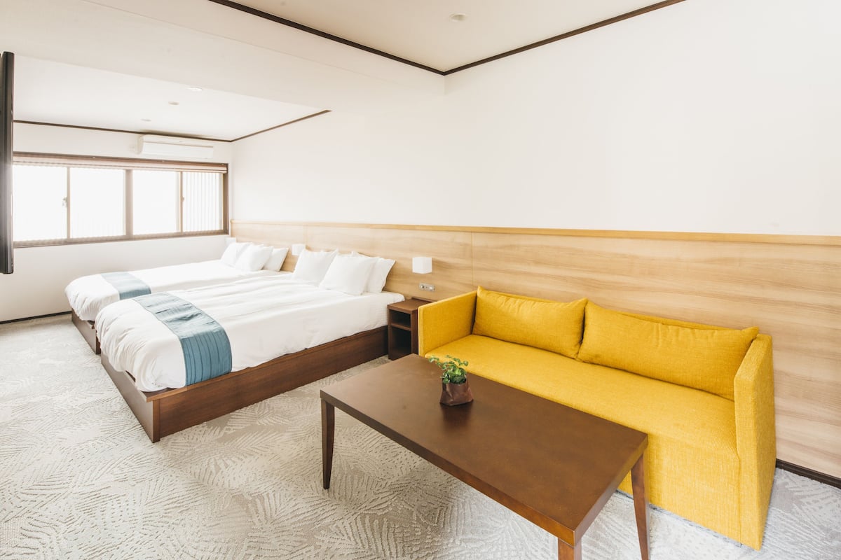 Une chambre d’hôtel avec un grand lit, un canapé, une table basse et une fenêtre avec des stores.