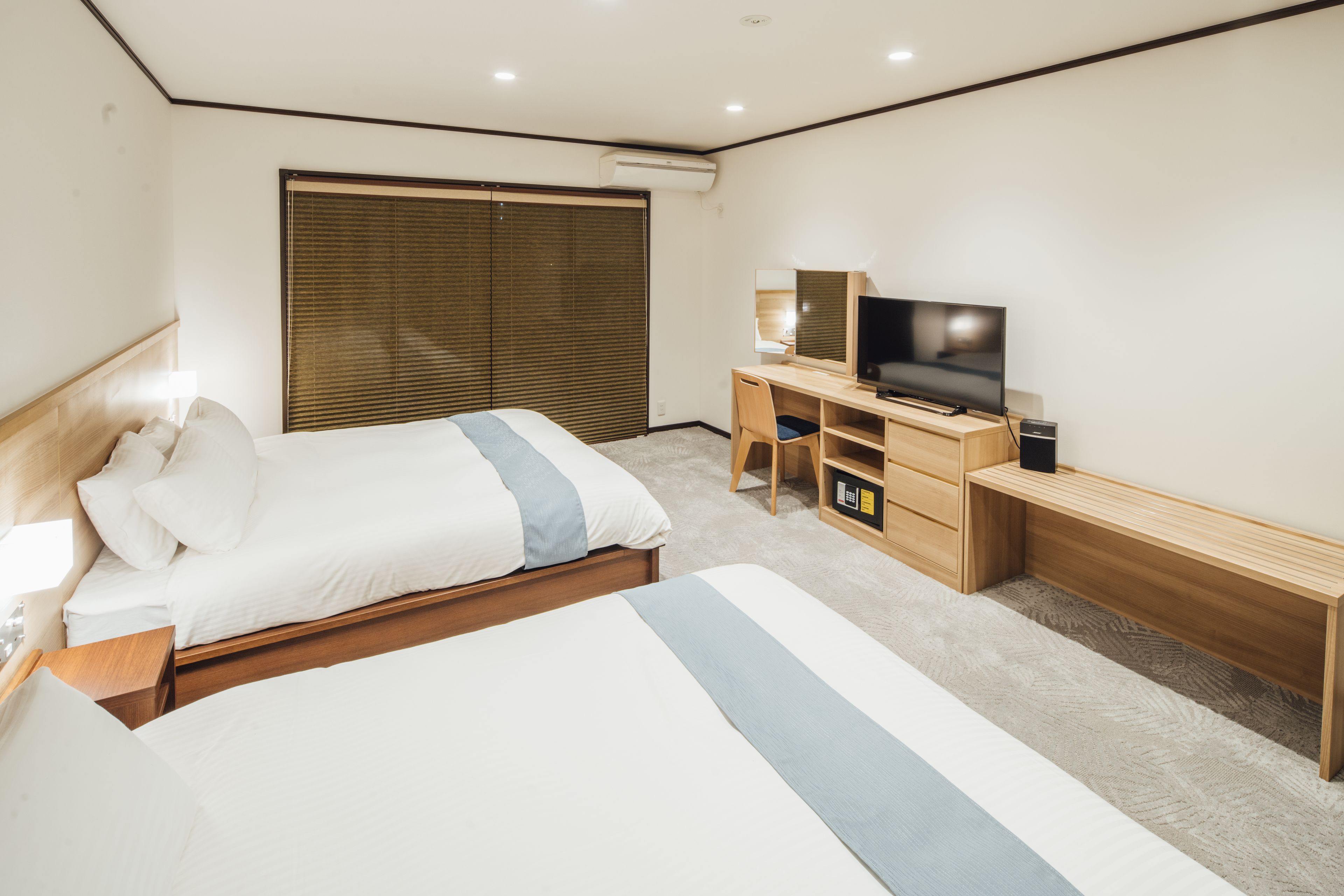 Quarto de hotel com uma cama grande, uma escrivaninha e uma televisão, além de uma porta de correr.
