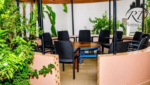 A round table with black chairs, surrounded by greenery and a tiled floor.