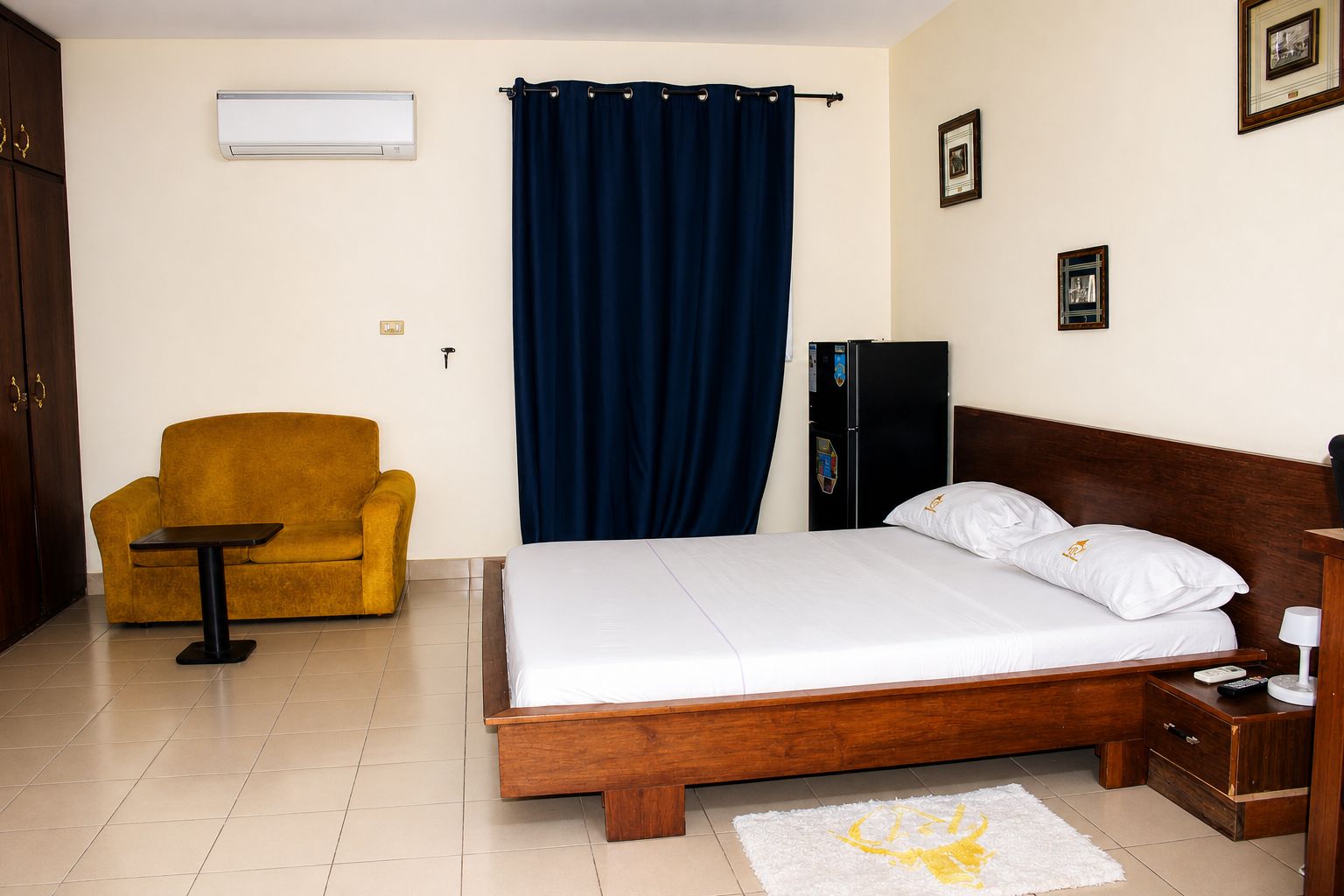 A hotel room with a bed, a sofa, a small table, a refrigerator, and a curtain.