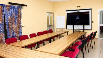 Un salón de conferencias con una larga mesa, sillas rojas, una pantalla de proyector y una pizarra.
