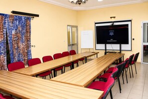 Un salón de conferencias con una larga mesa, sillas rojas, una pantalla de proyector y una pizarra.