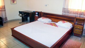 A neatly made bed with a wooden headboard, a bedside table with a lamp, and a chair. - Residence Diane (Ouagadougou)
