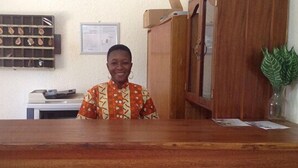 A reception area with a wooden desk, a bulletin board, and a framed notice on the wall. - Residence Diane (Ouagadougou)