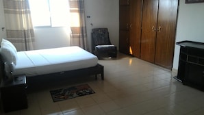 A bedroom with a bed, a chair, a wardrobe, and a desk. - Residence Diane (Ouagadougou)