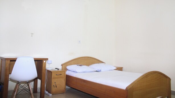 A bedroom with a wooden bed, a desk with a chair, and a small bedside table. - Residence Diane (Ouagadougou)