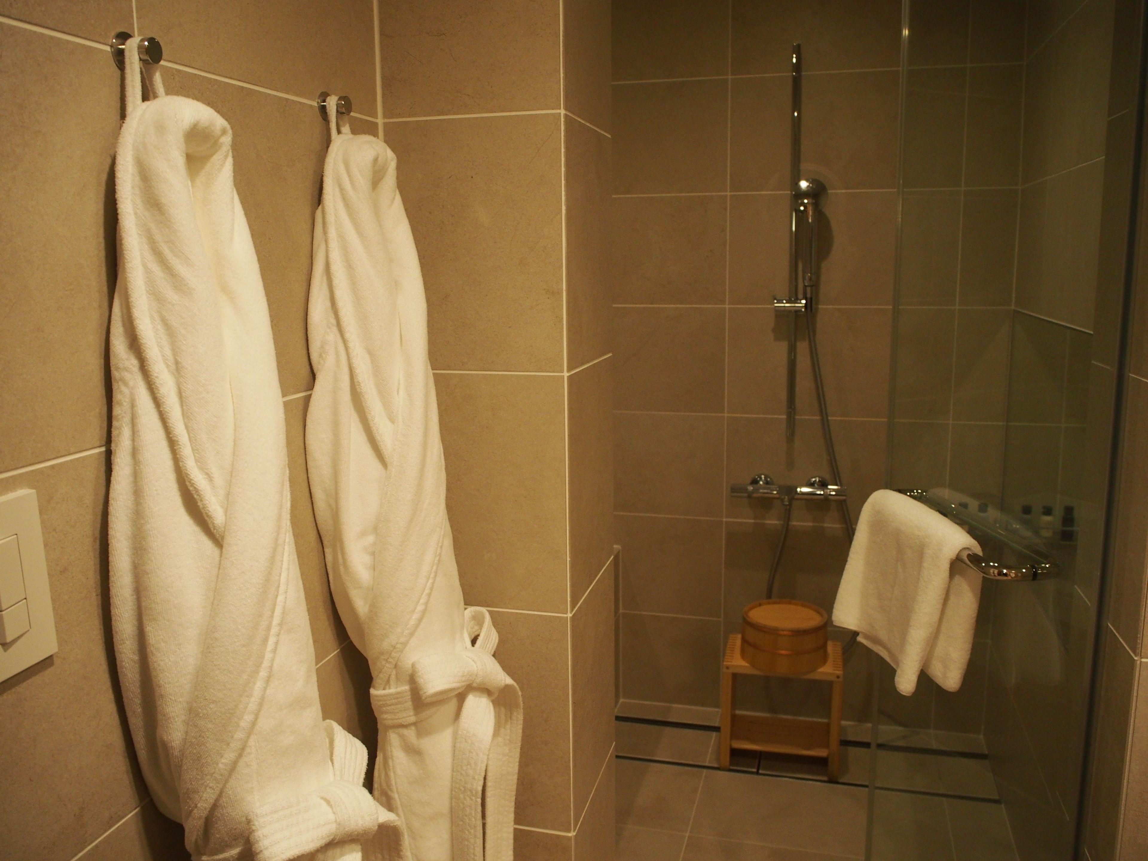 A bathroom with two white towels hanging on a rack, a shower with a glass door, and a wooden stool.