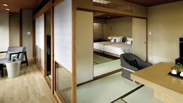 Una habitación de hotel al estilo japonés tradicional, con suelo de tatami, un escritorio de madera bajo, una cama con ropa blanca y una puerta corredera de shoji.