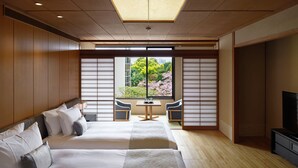 A hotel room with two beds, a TV, a small table, and a view of cherry blossoms through large windows. - Takanawa Hanakohro, a Member of Small Luxury Hotels of the World (Tokyo)