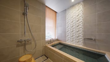 A modern bathroom with a freestanding bathtub, a showerhead, and a window with blinds.