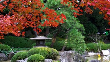 Un jardín japonés tradicional con un farol de piedra, arbustos cuidadosamente mantenidos y un estanque con rocas.